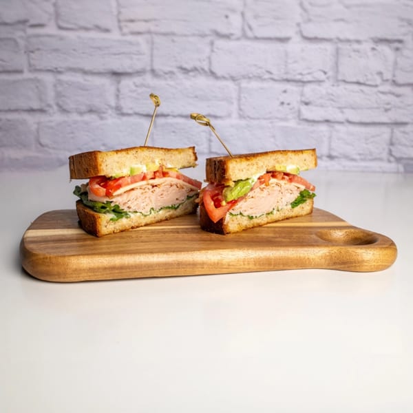 Two halves of a turkey club sandwich with avocado, tomato, and lettuce on a wooden board.