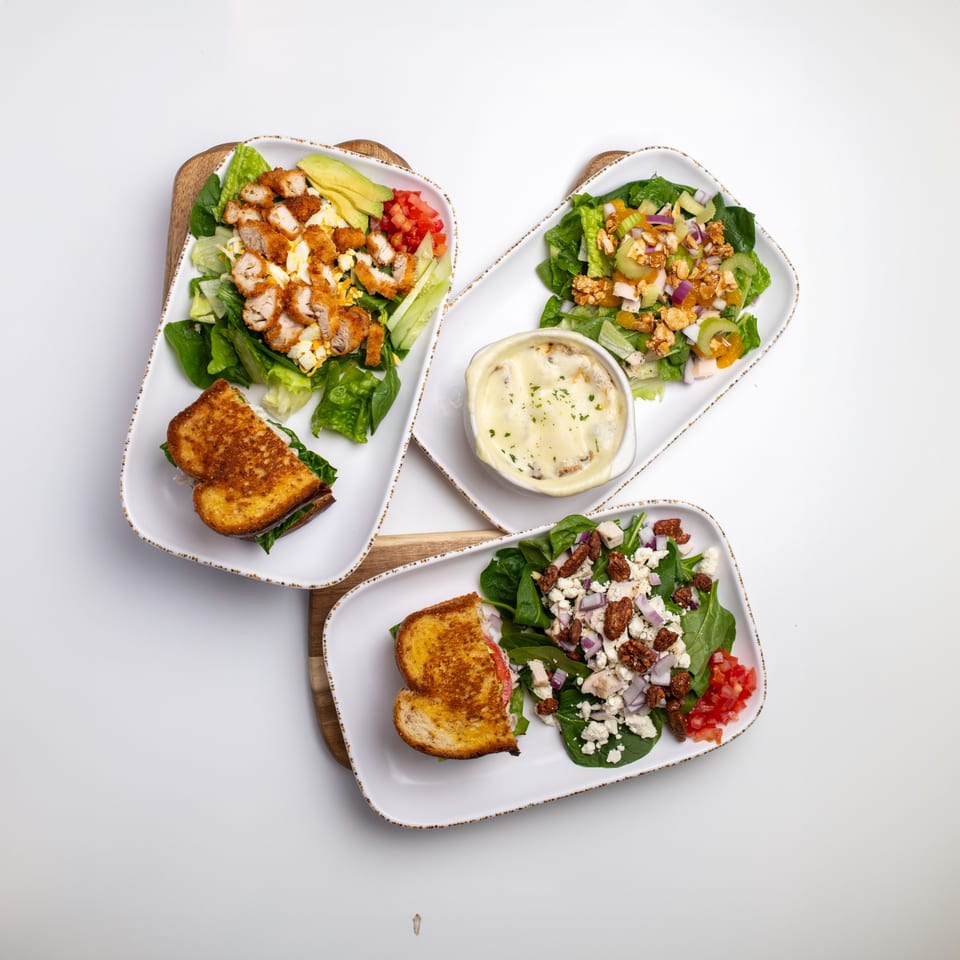Three American-style salads with grilled sandwiches and a bowl of French onion soup on white plates.