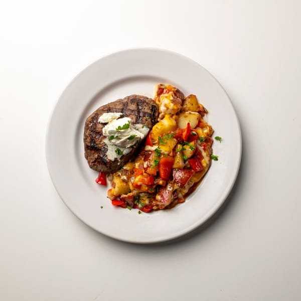 Grilled steak topped with white cheese and parsley, served with roasted potatoes and red peppers.