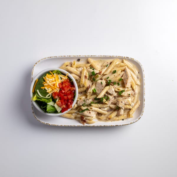 Creamy chicken penne pasta with a side salad topped with cheese and diced tomatoes.