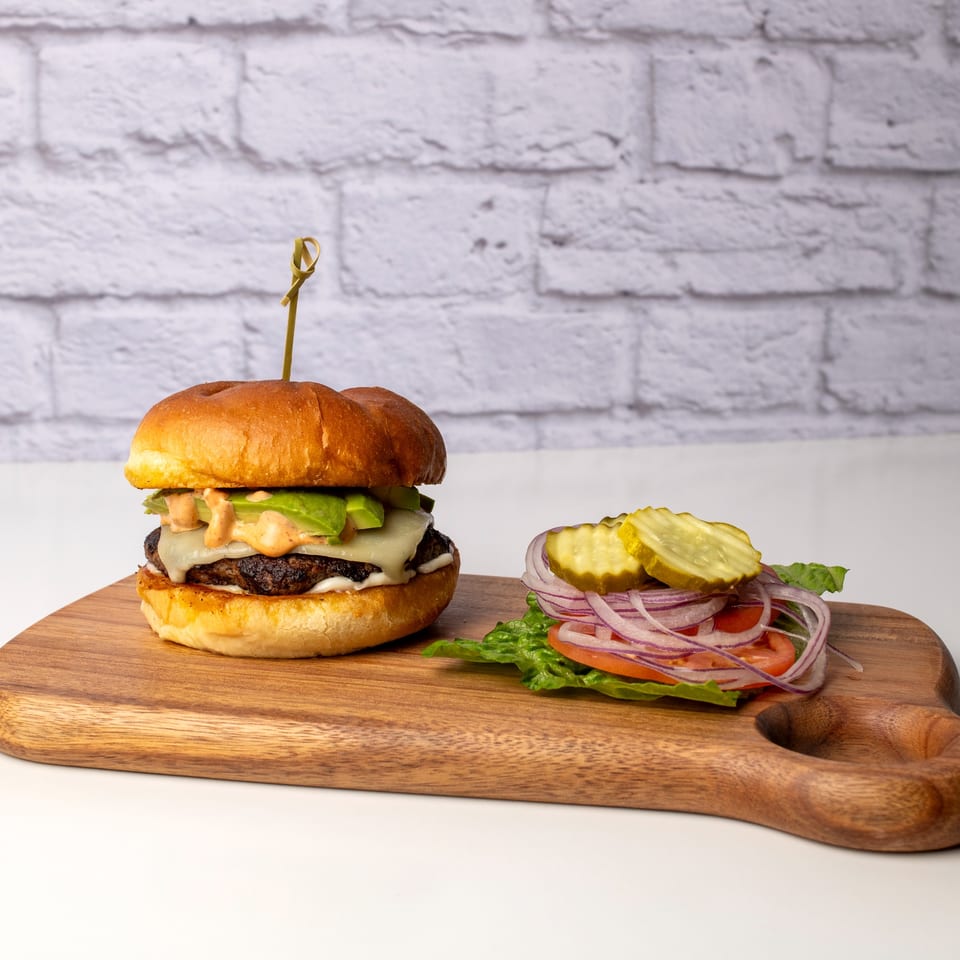 A Red Onion Cafe burger with avocado, cheese, and special sauce, alongside fresh toppings.